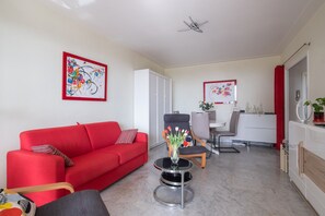 A modern living room with a red sofa, a round coffee table, and a dining area with a white cabinet and chairs.