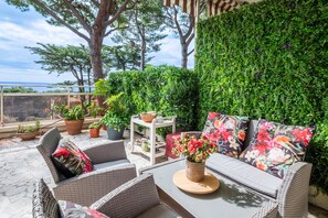 An outdoor seating area with wicker furniture, a table with a potted plant, and a wall covered in greenery.