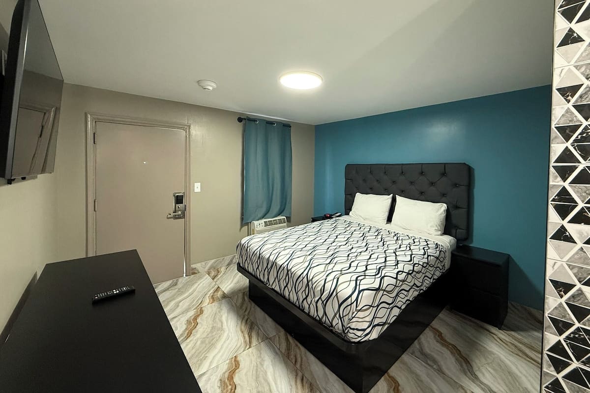 Quarto com cama, escrivaninha, televisão e porta.