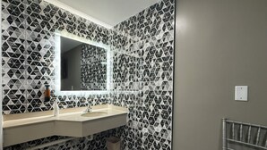 A bathroom with a geometric tile backsplash, a large mirror, a vanity with a sink, and a towel rack. - Beauty Rest Hotel (Edison)