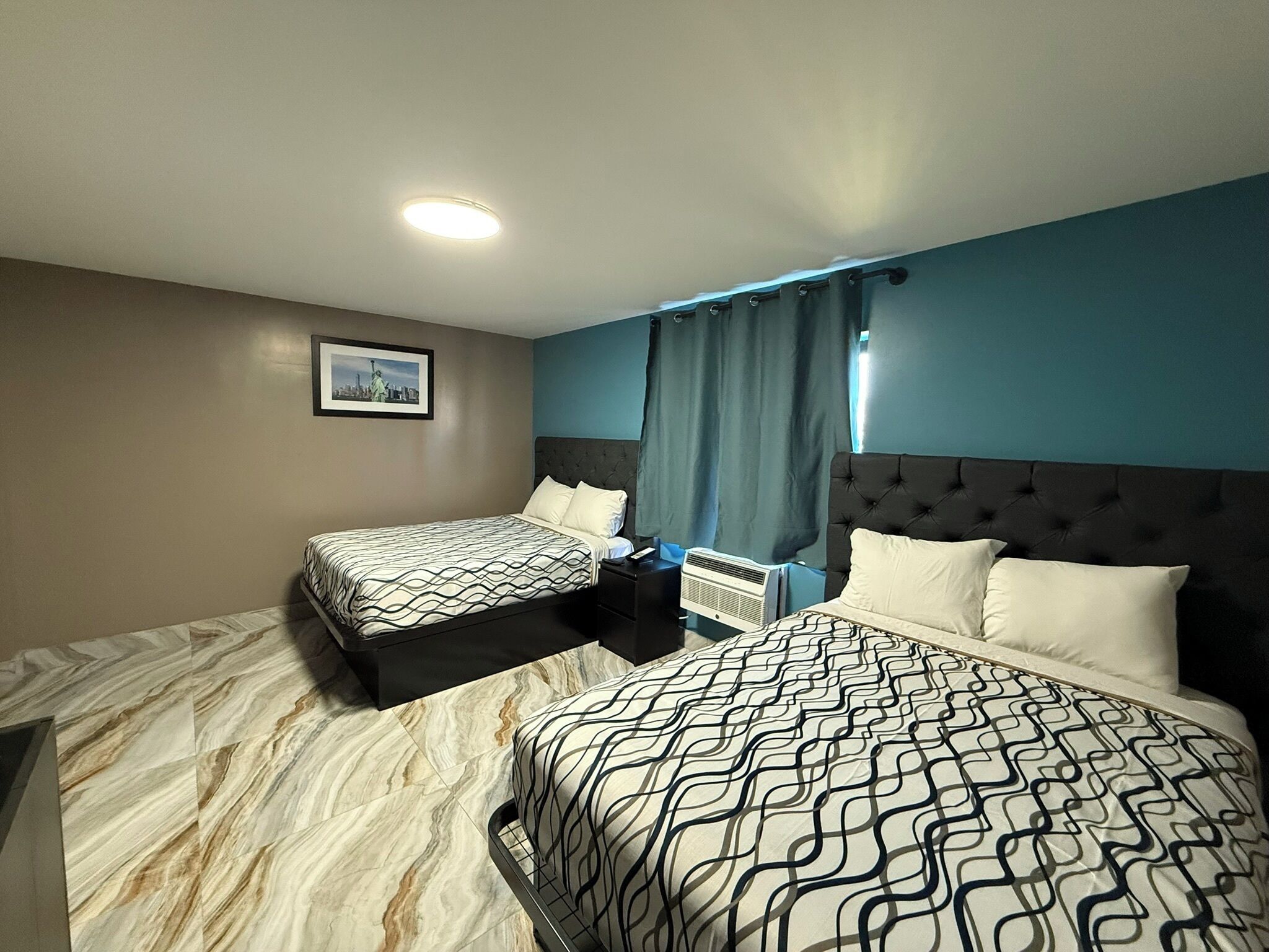 Habitación de hotel con dos camas, una mesita de noche, un cuadro en la pared y una lámpara en el techo.