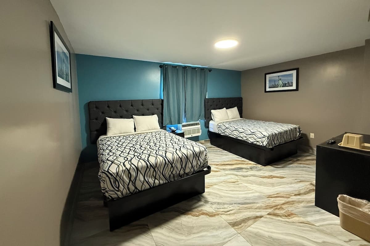 Quarto de hotel com duas camas, uma escrivaninha e um cesto de lixo.