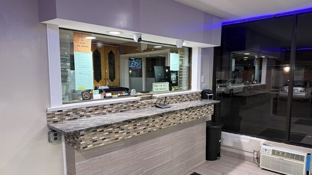 A modern reception desk with a tiled counter, a large mirror, and a glass door leading outside. - Beauty Rest Hotel (Edison)