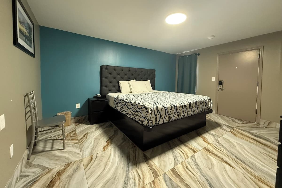 Quarto com cama de cabeceira estofada, mesa de cabeceira com telefone e porta de banheiro.