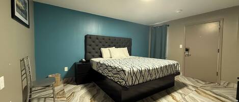 A bedroom with a tufted headboard bed, a bedside table with a phone, and a bathroom door.