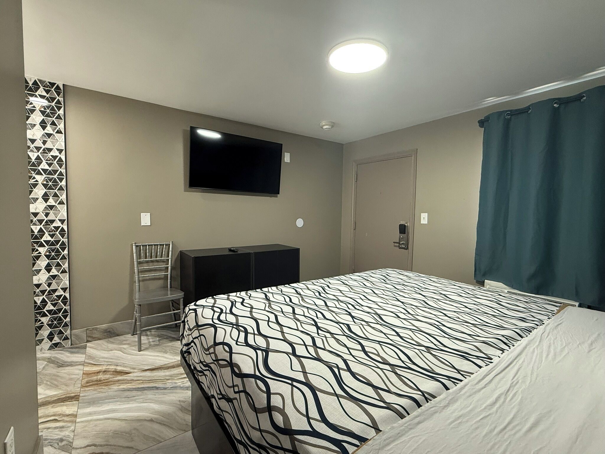 A hotel room with a bed, a TV mounted on the wall, a desk, and a chair.