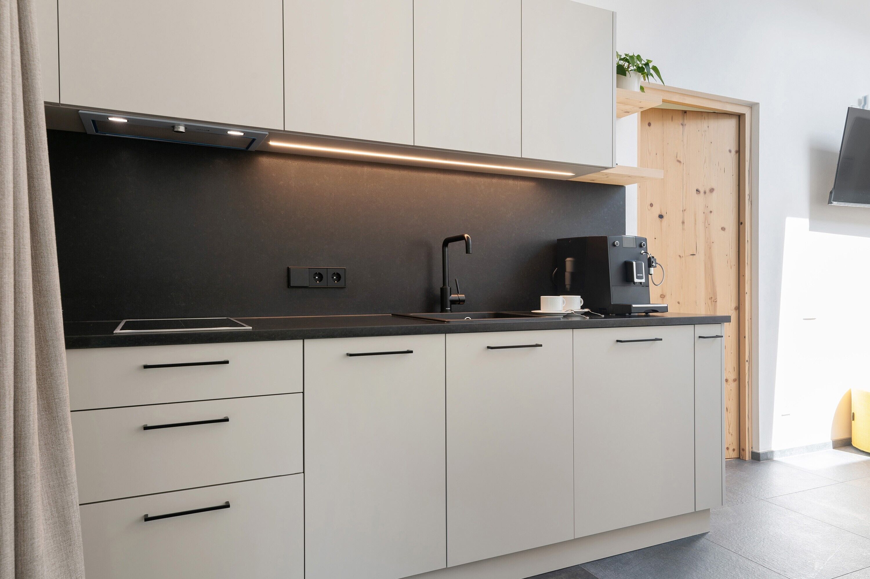 A modern kitchen with a black countertop, white cabinets, a coffee machine, and a wooden door.