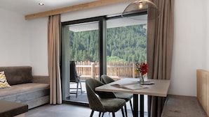 Una habitación moderna con sofá, mesa de comedor, sillas y vistas a una zona boscosa a través de grandes ventanales.