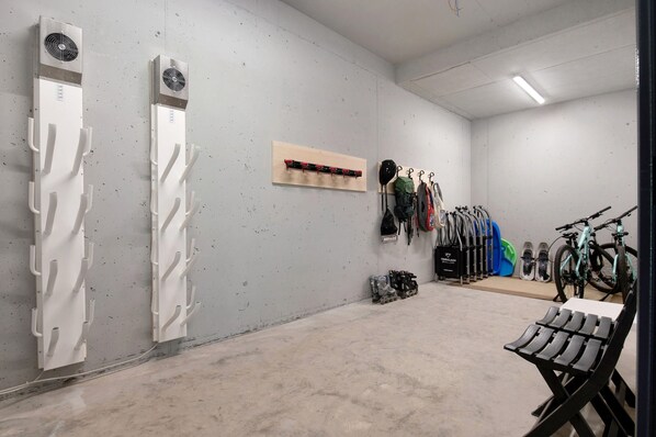 Una habitación limpia y moderna con piso de concreto, dos unidades de aire acondicionado fijadas a la pared, un perchero de madera, un área de descanso y una bicicleta.