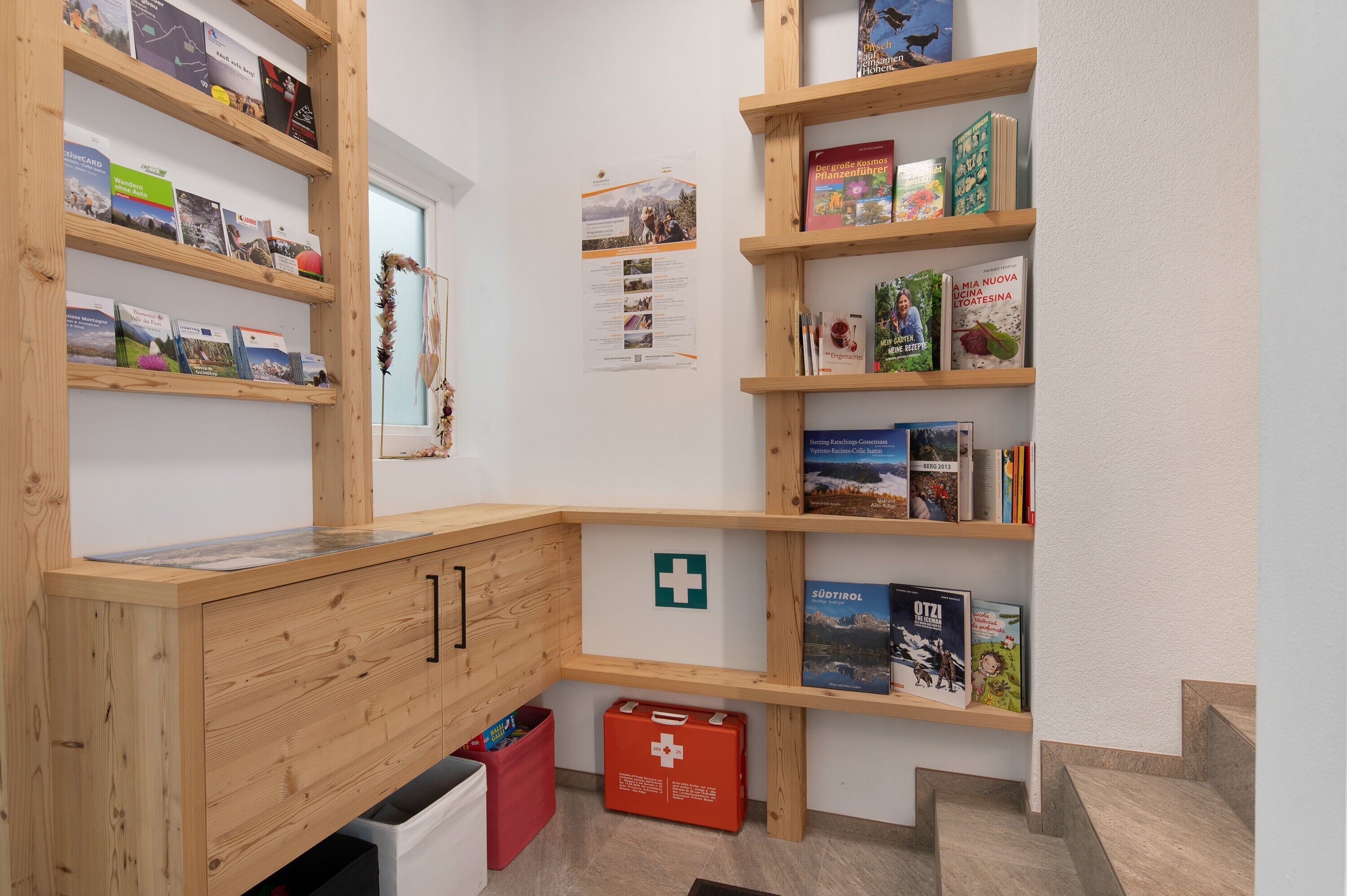 Ein Eckzimmer mit Holzregalen, auf denen Bücher und eine rote Erste-Hilfe-Ausrüstung stehen.