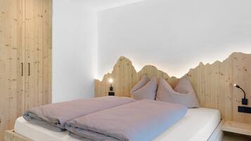 A bedroom with a wooden headboard, two beds, bedside tables, and a wall-mounted lamp.