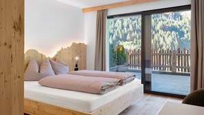 Camera da letto con testiera in legno, letto con biancheria rosa, comodino e vista su una foresta attraverso una porta scorrevole in vetro.