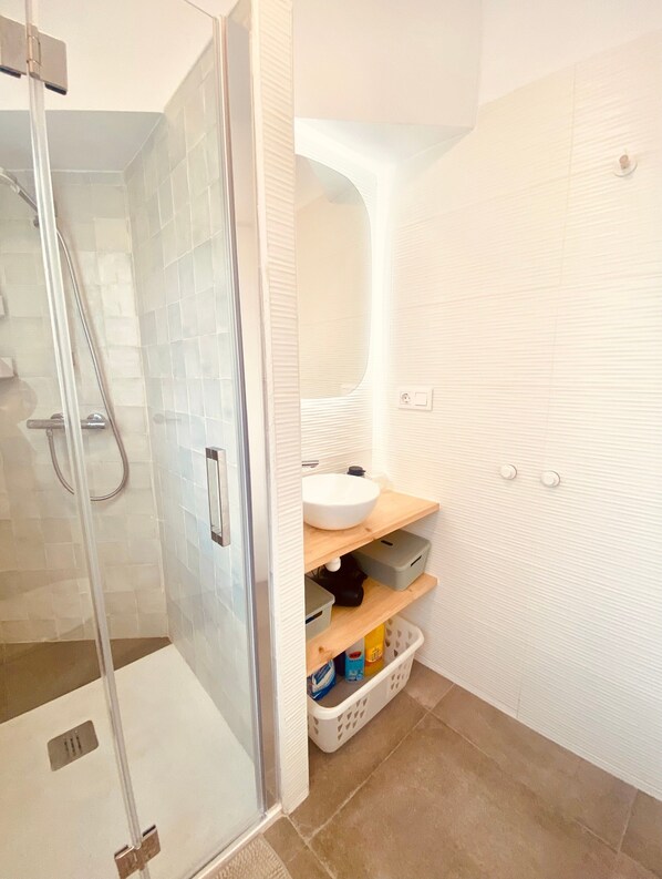 Un baño con cabina de ducha de vidrio, un lavabo blanco y un espejo.