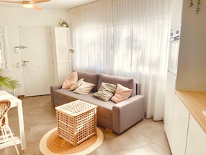 Un salon avec un canapé, une petite table en bois, un fauteuil en osier et une porte.