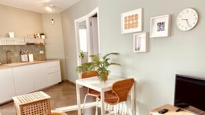 A modern kitchen with white cabinets, a dining table with wicker chairs, a TV stand, and a wall clock.