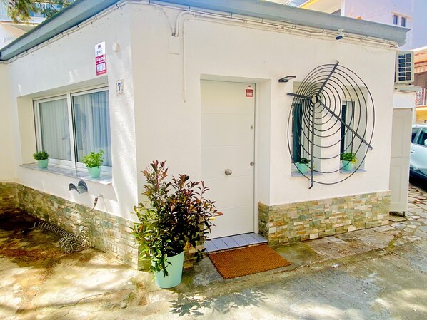 Un pequeño edificio con fachada blanca, una puerta, ventanas y una escalera de caracol.