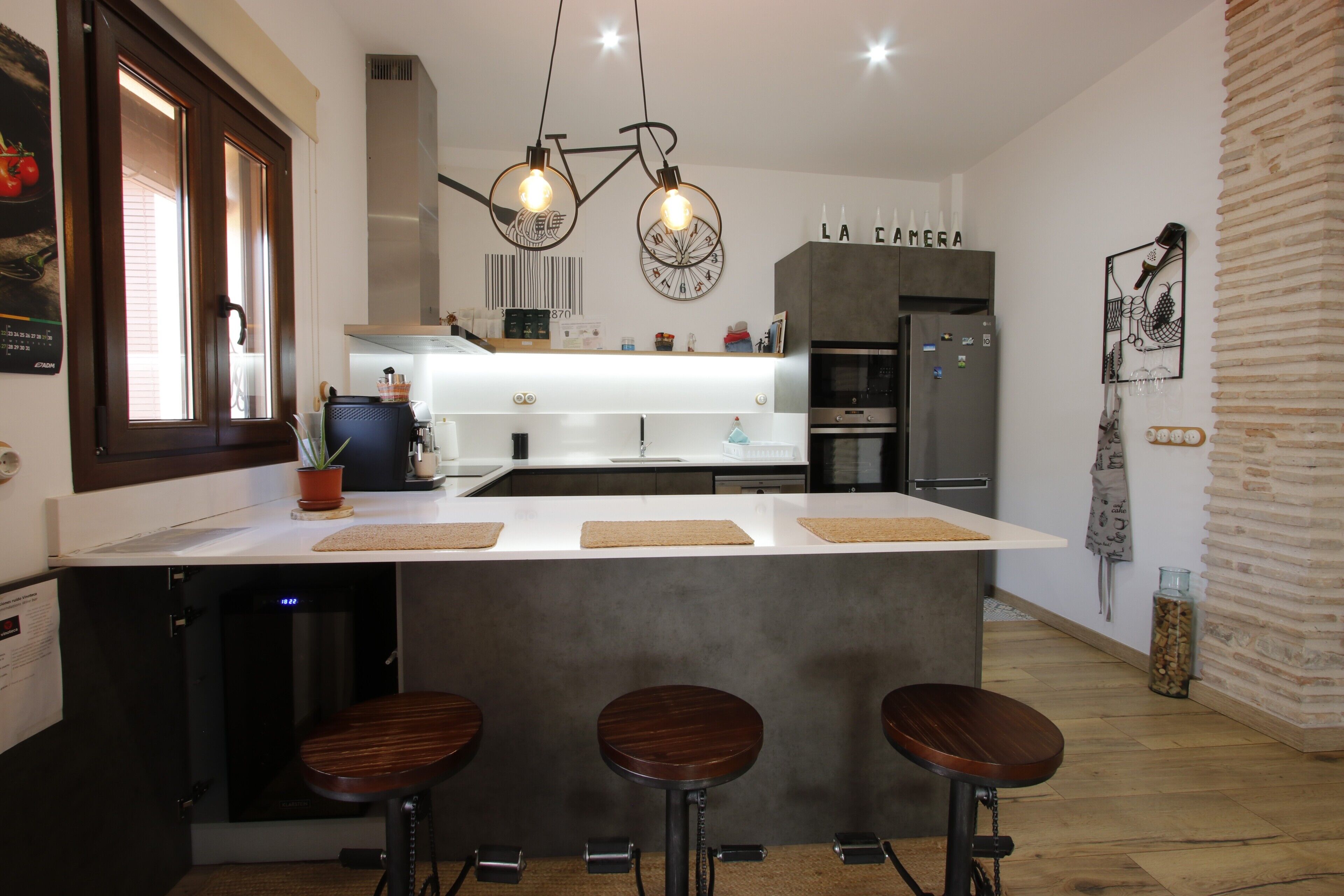 Una cocina moderna con una isla central, taburetes de bar y un refrigerador.