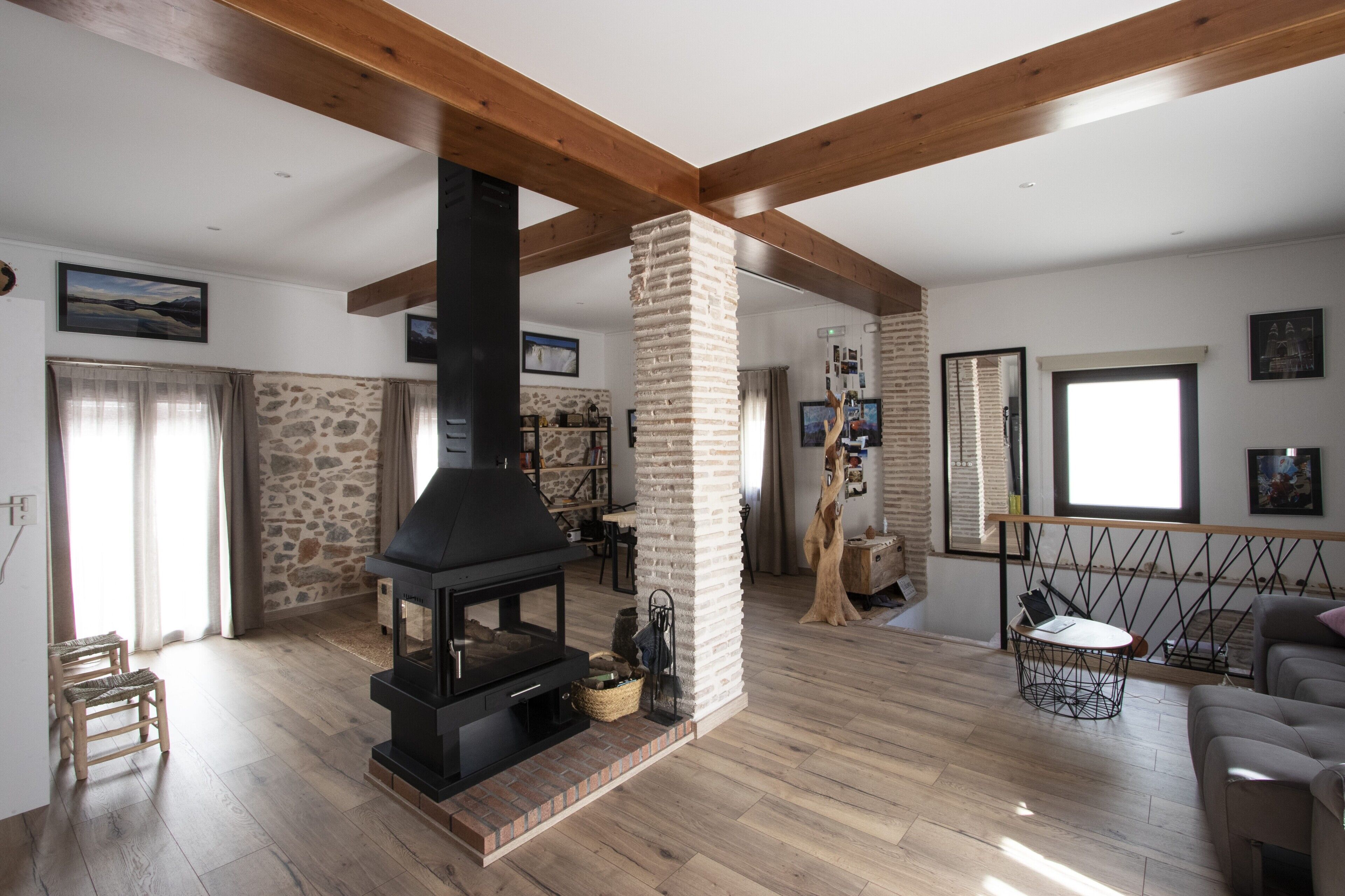 A living room with a fireplace, wooden beams, stone wall, and a view of the outdoors.