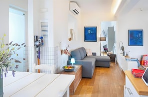 En moderne stue med en grå sofa, et spisebord og et køkkenområde med en vanddispenser.