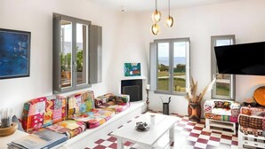 Een woonkamer met een kleurrijke bank, een witte salontafel, een open haard en een groot raam met uitzicht.