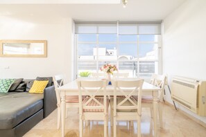 Een moderne woonkamer met een eettafel, witte stoelen, een grijze bank en een groot raam.