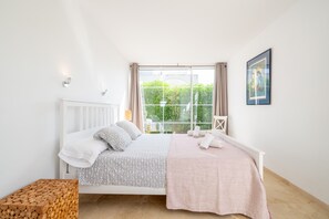 Een slaapkamer met een bed, een raam met gordijnen, een nachtkastje en een ingelijst schilderij aan de muur.