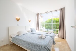 Een hotelkamer met twee bedden, een groot raam met gordijnen en uitzicht op groen.