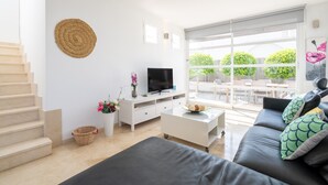 A modern living room with a staircase, a flat-screen TV, a white sofa, and a large window with a view of greenery. - Holiday Home 'Marc 6' with Private Pool, Wi-Fi and Air Conditioning (Can Picafort)