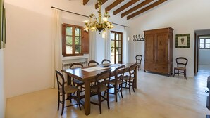 A dining area with a wooden table and chairs, a chandelier, and a large wooden cabinet. - Country House 'Calma' with Mountain View, Private Pool and Wi-Fi (Illes Balears)