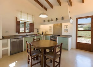 Uma cozinha com mesa de jantar, cadeiras, lava-louças, fogão e janela com persianas.