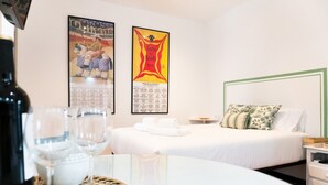 Une chambre d’hôtel avec un lit, une table sur laquelle se trouvent des verres et une bouteille, et deux affiches accrochées au mur.