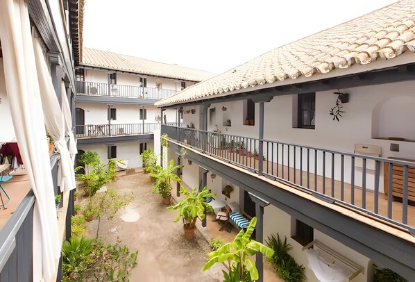 A courtyard with potted plants, balconies, and a tiled roof.