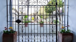 Un portail en fer forgé, agrémenté d’un motif décoratif, qui donne sur une zone pavée où sont disposées des plantes en pot.