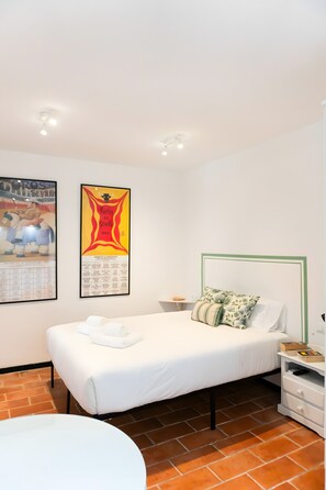 A bedroom with a bed, a nightstand, a pillow, a wall calendar, and a round table.
