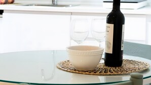 Une table en verre sur laquelle se trouvent une bouteille de vin, deux verres et un bol, le tout posé sur un set de table blanc.