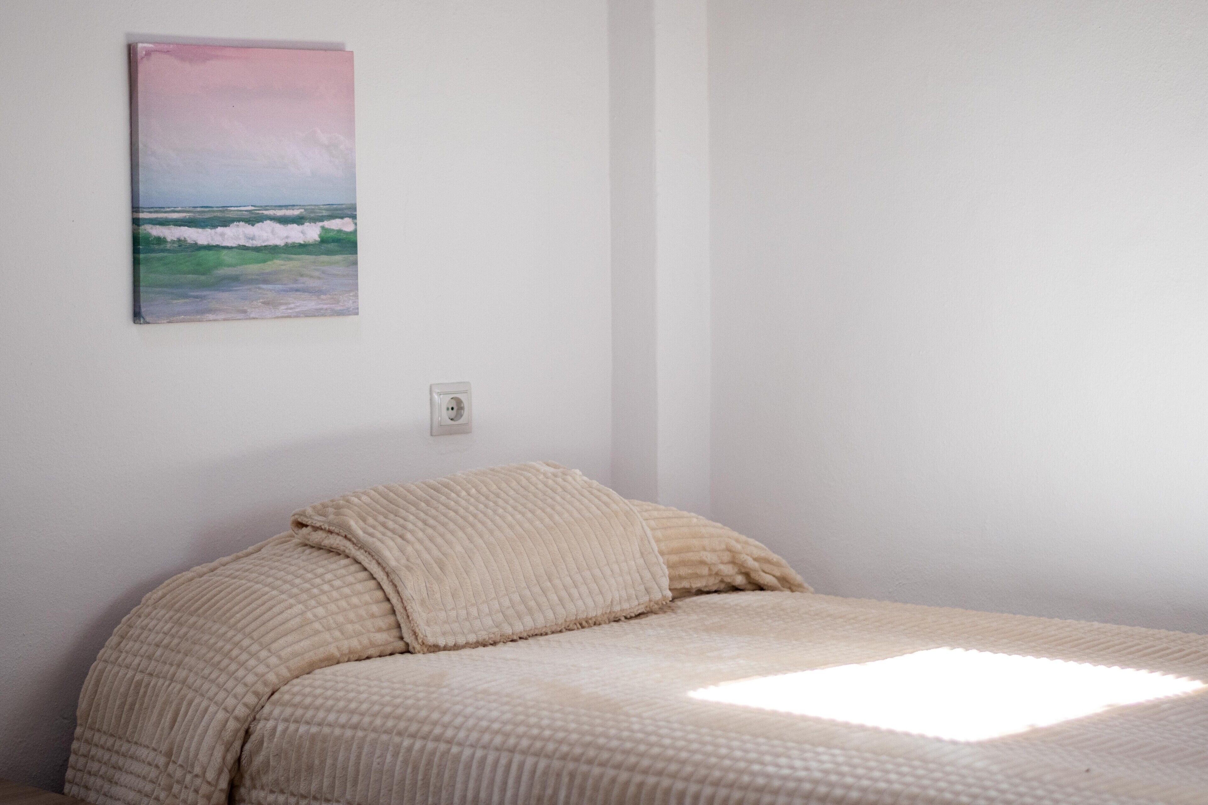 A bedroom with a bed, a painting, and a wall socket.