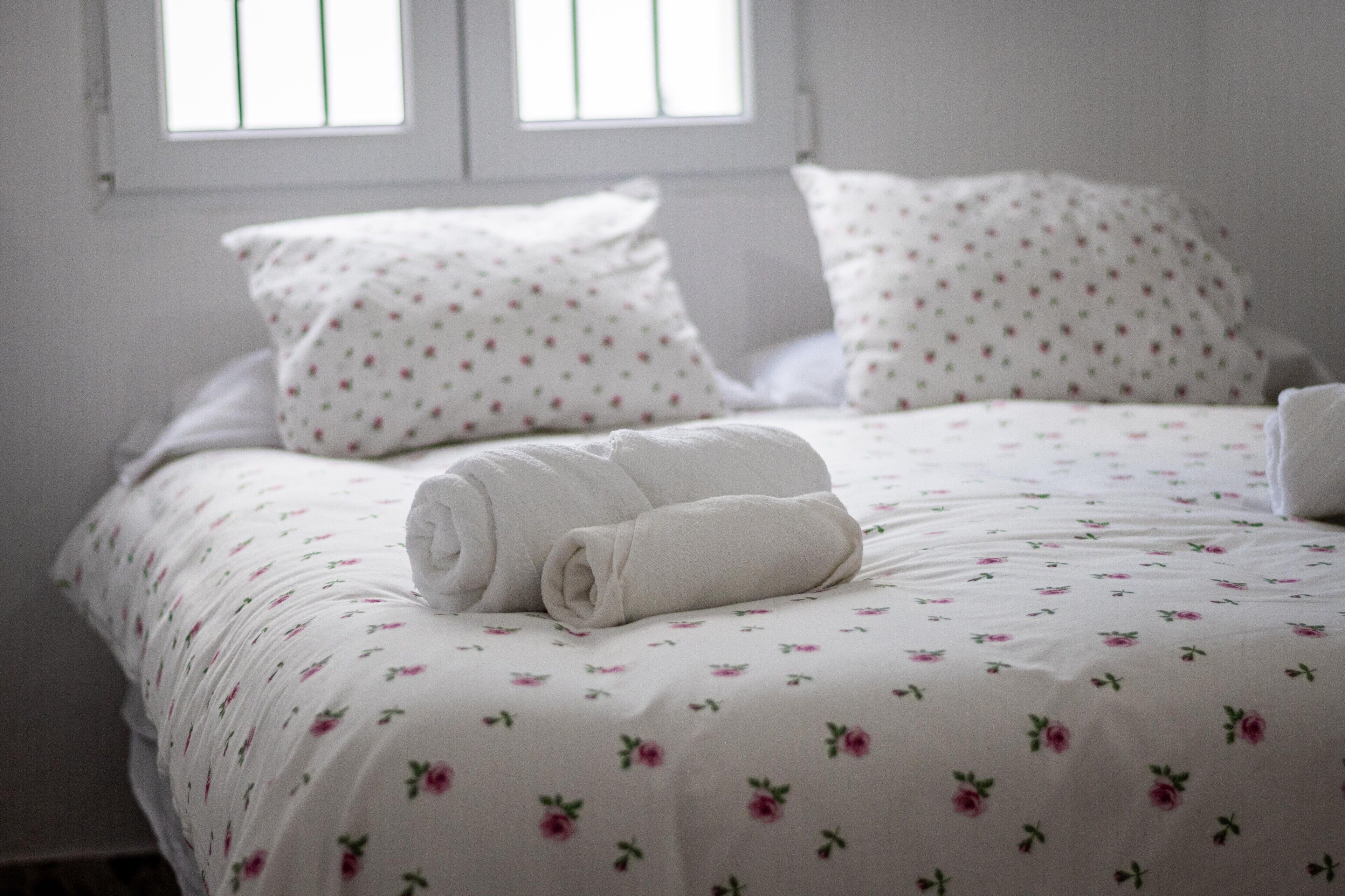A neatly made bed with floral bedding, pillows, and a rolled towel.