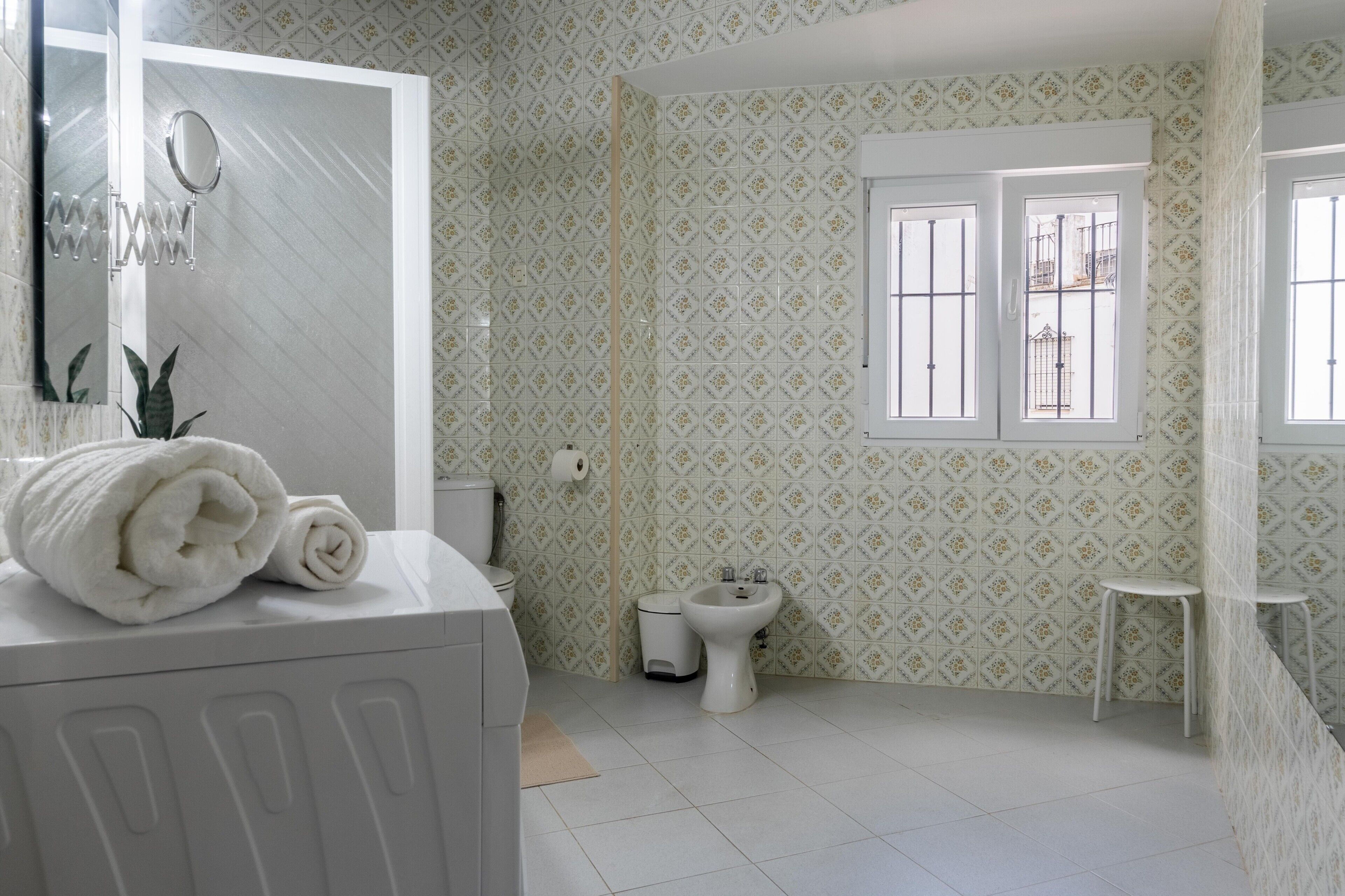 A bathroom with patterned wallpaper, a toilet, bidet, and a mirror.
