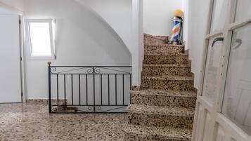 Una escalera con piso de terrazo que lleva a un rellano, una barandilla de metal y un palo de barbero.