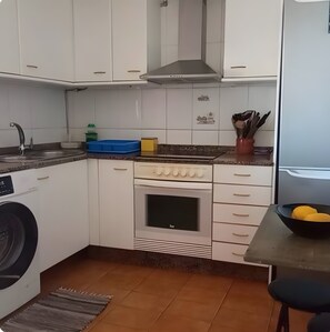 Una cocina compacta con armarios blancos, horno empotrado, lavadora y un comedor con mesa y sillas.