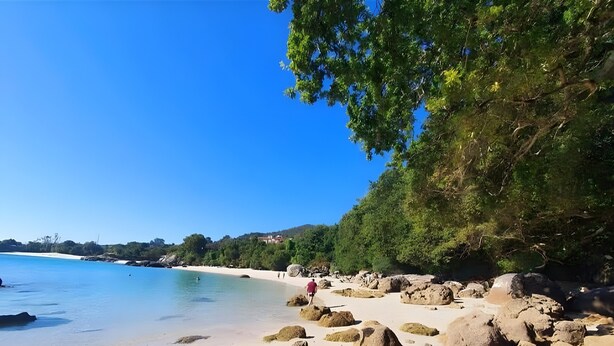 A beach with large rocks, clear blue water, and a person walking. - Holiday Home 'Villa Lukita' with Sea Views, Wi-Fi and Air Conditioning (Cangas)
