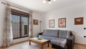 Ein Wohnzimmer mit einer Couch, einem Couchtisch, einem Fenster mit Vorhängen und Wandbildern.