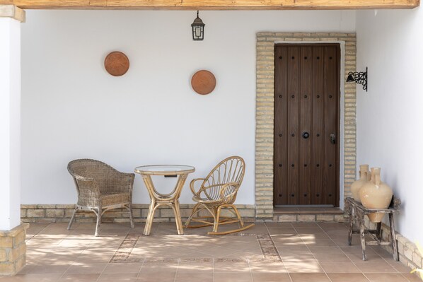 Une terrasse dotée de meubles en osier, d’une porte en bois et d’assiettes décoratives accrochées au mur.