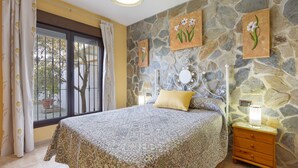 Ein Schlafzimmer mit einem Bett, einem Nachttisch, einer Lampe und einer Steinwand.