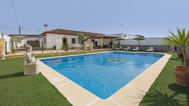 Ein Swimmingpool mit Fliesenrand, eine Buddha-Statue und ein Haus mit einem Ziegeldach.