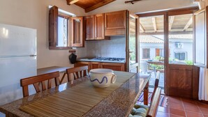Une cuisine avec des meubles en bois, une table à manger avec un set de table, et une vue sur l’extérieur par une porte ouverte.
