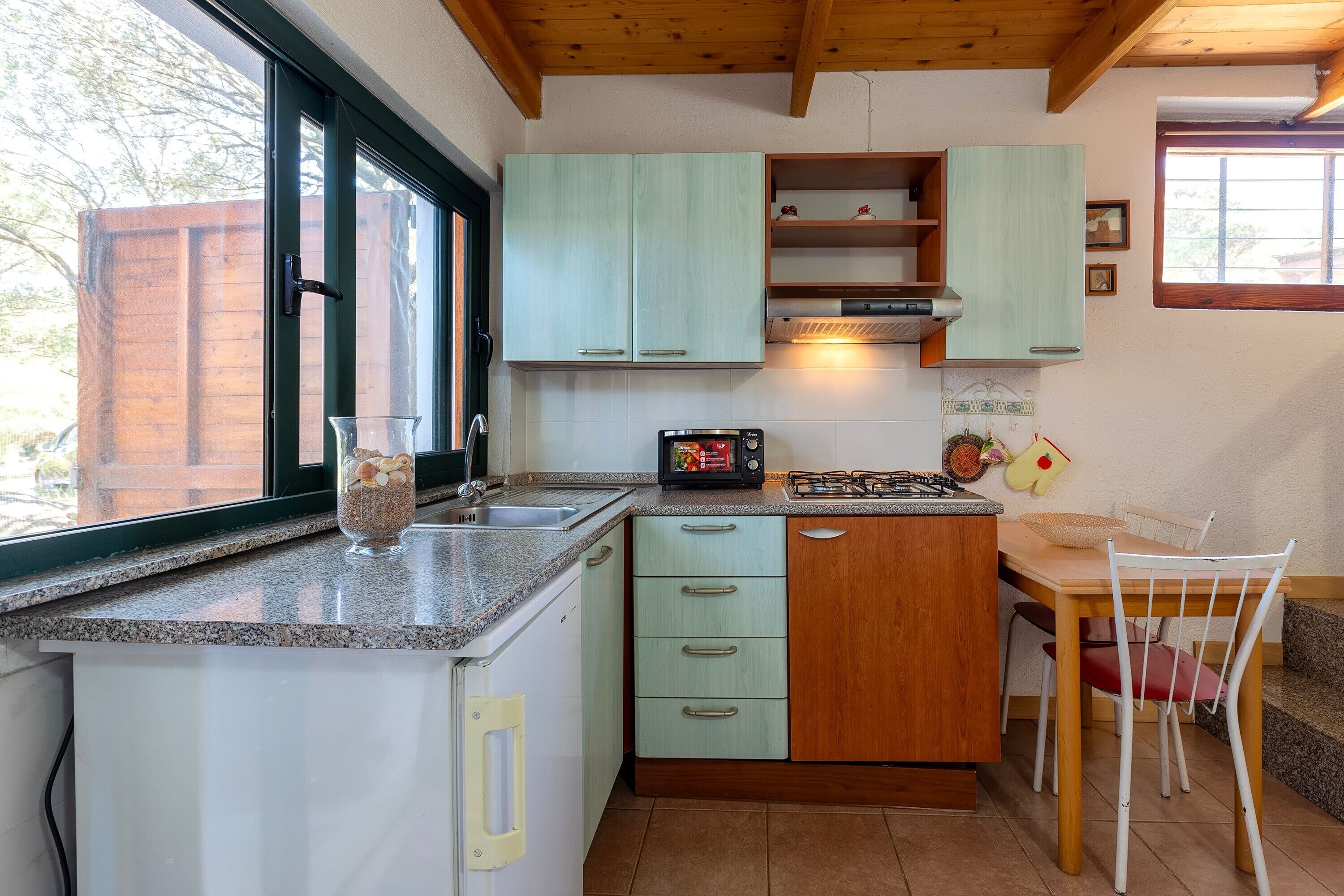 A kitchen with a window, a microwave, a sink, and a dining area with chairs.