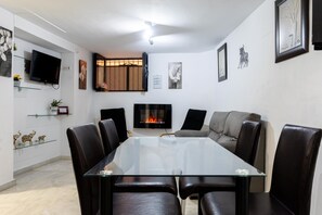 A modern living room with a glass-top dining table, leather chairs, a fireplace, and wall-mounted artwork.