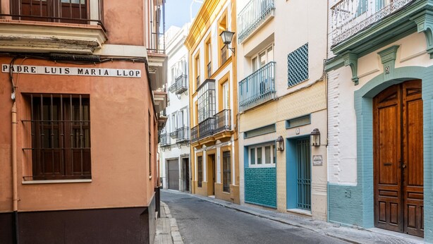 A narrow street lined with colorful buildings, including a building with a sign reading 'PERE LUIS MARIA LLOP.'