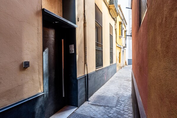 A narrow alleyway with buildings on either side, a door on the left, and a metal grate on the ground.